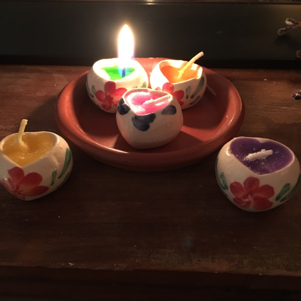 Several tiny hear-shaped candles with colorful flower decorations burn cheerfully on a mantle.